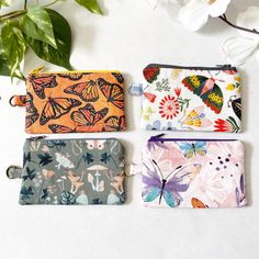 three small zippered pouches sitting next to each other on a white surface with flowers in the background