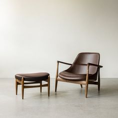 a chair and ottoman sitting on the floor in front of a white wall with a brown leather cushion