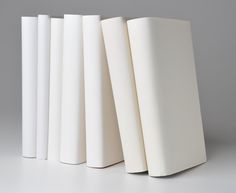 four white books are lined up against each other on a gray surface, with one book in the foreground