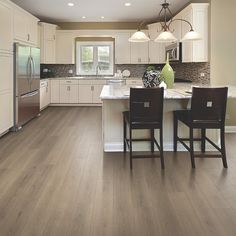 a large kitchen with white cabinets and wood flooring, along with two bar stools