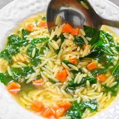 a white bowl filled with pasta and spinach on top of a table next to a spoon