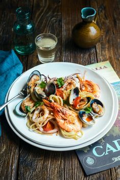 a white plate topped with pasta and clams on top of a wooden table next to glasses