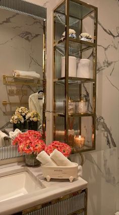 a white sink sitting under a mirror next to a shelf filled with towels and flowers