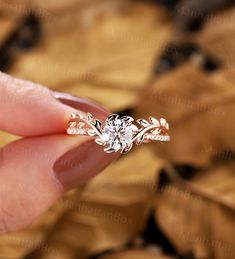 a woman's hand holding an engagement ring with leaves around it and the center stone in