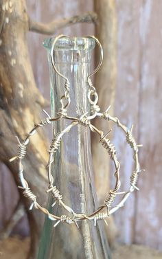 a glass vase filled with lots of silver wire wrapped around it's sides and hanging from a tree branch