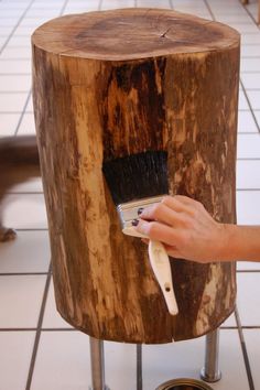 a person using a brush to paint a tree stump stool with white tile on the floor