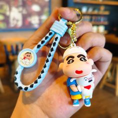 a hand holding a keychain with a cartoon character on the front and back