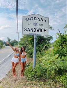 two women standing in front of a sign on the side of the road that says entering sandwich