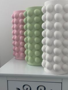 three different colored vases sitting on top of a white dresser next to a clock