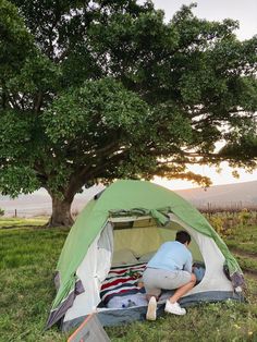 a man sitting in front of a tent under a tree with his feet on the ground