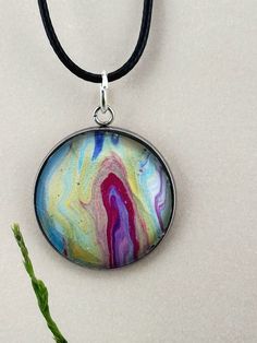 a necklace with an oval pendant hanging from it's side on a black cord