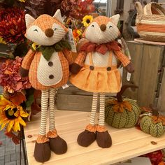 two stuffed foxes dressed in orange and brown outfits, standing next to each other on a table