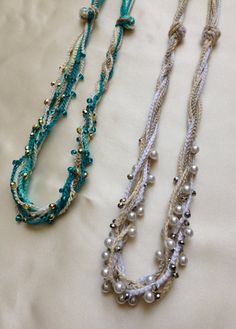 three necklaces are laying on a white sheet and one is blue, the other has silver beads