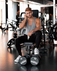 a man sitting in a gym chair talking on a cell phone while holding a pair of dumbbells