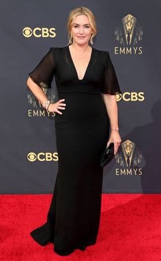 a woman in a black dress on the red carpet at an awards event with her hands on her hips