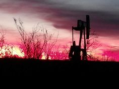 an oil pump at sunset with trees in the foreground and clouds in the background