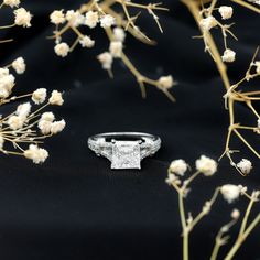 a diamond ring sitting on top of a black cloth next to white flowers and branches