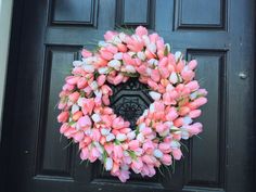 a wreath with pink and white tulips is hanging on the front door,