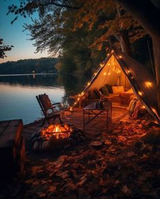 a tent that is next to the water with some chairs around it and lights on