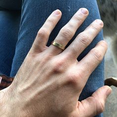 a person's hand with a ring on their finger and a cat in the background