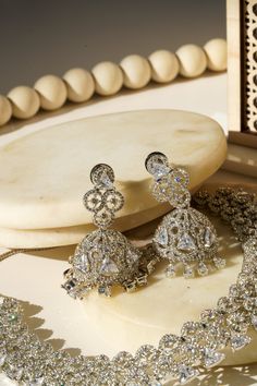 Elevate your allure with the Zeba - Classic AD Necklace Set adorned with Jhumka Earrings, a timeless piece crafted for sophistication. Available in two enchanting finishes, Rhodium (silver finish) or Gold plated, this set boasts intricate patterns of white AD stones, weaving triangular cut stones amidst circular designs created with smaller AD stones throughout. The accompanying lightweight Jhumka earrings, approximately 2 inches in length, exude elegance and boast a brilliant sparkle, adding a Jhumka Earrings, Rhodium Plated, Timeless Pieces, Necklace Set, Silver Plate, Gold Earrings, Gold Plate, Sparkle, Stone