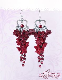 a pair of earrings with red flowers hanging from it's earwires on a pink background