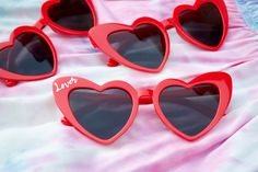 red heart shaped sunglasses with the word love written on them sitting on a pink blanket