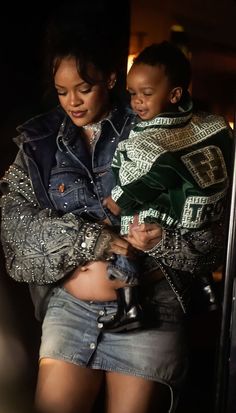 a woman holding a child in her arms while standing next to a man wearing a jacket