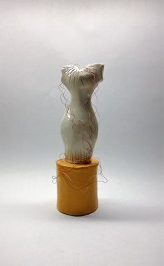 a white ceramic sculpture sitting on top of a yellow container filled with string wrapped around it