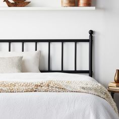 a bed with white linens and pillows in a small room next to two shelves on the wall