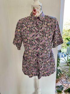 "Vintage 1960s blouse in a ditsy flower pattern. The blouse has a nice rounded Peter Pan collar and nice details at the pockets. The blouse has small shoulder pads to shape it. The blouse is closed with purple plastic buttons. The blouse is in good condition. The fabric seems to be a good quality cotton. There is no tags but I estimate the size to be a M.  Please check measures below. Measured with buttons closed and laid flat. Armpit to armpit: 50 cm - 19,7\" Waist: 45 cm - 17,7\" Lenght: 64 cm - 25,2\"" Floral Print Short Sleeve Work Shirt, Short Sleeve Floral Print Shirt For Work, Short Sleeve Shirt With Retro Print For Spring, Workwear Floral Print Short Sleeve Shirt, Vintage Short Sleeve Blouse With Retro Print, Retro Short Sleeve Top With Vintage Pattern, Floral Print Short Sleeve Blouse For Work, Fitted Short Sleeve Shirt With Retro Print, Short Sleeve Blouse With Floral Print For Work