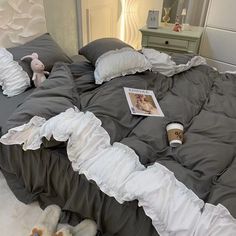 an unmade bed with white ruffles and grey comforter on top of it