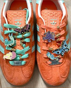 an orange adidas sneak with colorful butterflies on the front and side, sitting on a wooden floor