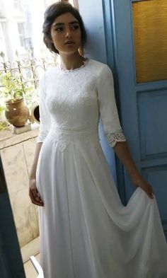 a woman standing in front of a blue door wearing a white dress with lace on it