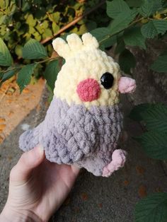 a hand holding a small crocheted bird on top of a leaf covered ground