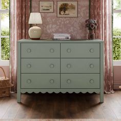 a green dresser sitting next to a window with pink curtains and pictures on the wall