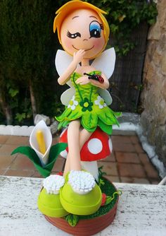 a little fairy figurine sitting on top of a mushroom with a flower in her hand