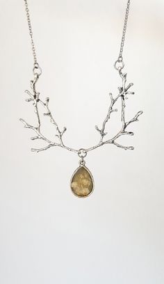 Enchanted Twig Necklace featuring two metal silver branches adorned with a teardrop pendant that holds a secret: a magical dried herb that has amazing powers! This necklace is for nature lovers, that appreciate some woodland flair, mixed with modern simplicity.  The beautiful old silver pendant has a milky thristle plant on its back and casted in a vintage looking resin, some dried flowers. The resin is milky and cloudy, just like an old, vintage painting. This ads character and a romantic look. Nature-inspired Silver Teardrop Jewelry, Silver Teardrop Necklace For Festivals, Silver Teardrop Necklace For Festival, Festival Silver Teardrop Necklaces, Hand-forged Silver Nature-inspired Necklace, Silver Teardrop Pendant Necklace Nature-inspired, Silver Nature-inspired Teardrop Pendant Necklace, Nature-inspired Silver Metal Necklace, Collectible Silver Necklace Nature-inspired