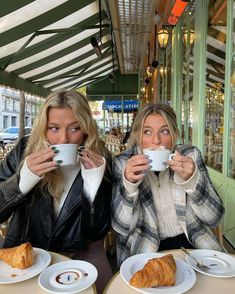 two women sitting at a table drinking coffee and croissants