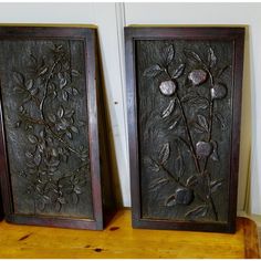 two metal framed pictures sitting on top of a wooden shelf next to eachother