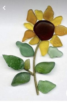 a sunflower made out of sea glass sitting on top of a white table next to green leaves