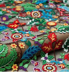 an embroidered fabric with colorful flowers and leaves on grey background, close - up photo