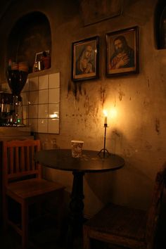 a small table with a candle on it in a dimly lit room next to two framed pictures