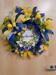 a welcome wreath with yellow and blue ribbons hanging on the front door to someone's home