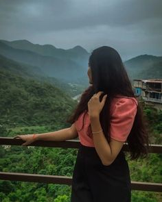 a woman standing on top of a balcony next to a lush green forest covered hillside