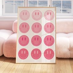 a framed poster with pink smiley faces on it in front of a couch and window