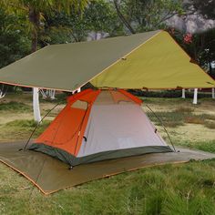 an orange and green tent sitting on top of a lush green field next to trees