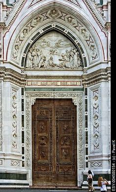 two people sitting on a bench in front of a large wooden door that has carvings all over it