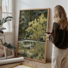 a woman standing next to a painting holding a glass of red wine in her hand