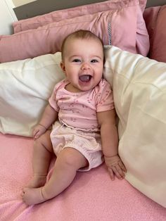 a baby sitting on top of a bed with pink sheets and pillows in front of it